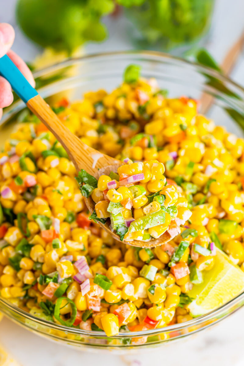 scoop of tex-mex corn salad on a wooden spoon over the bowl