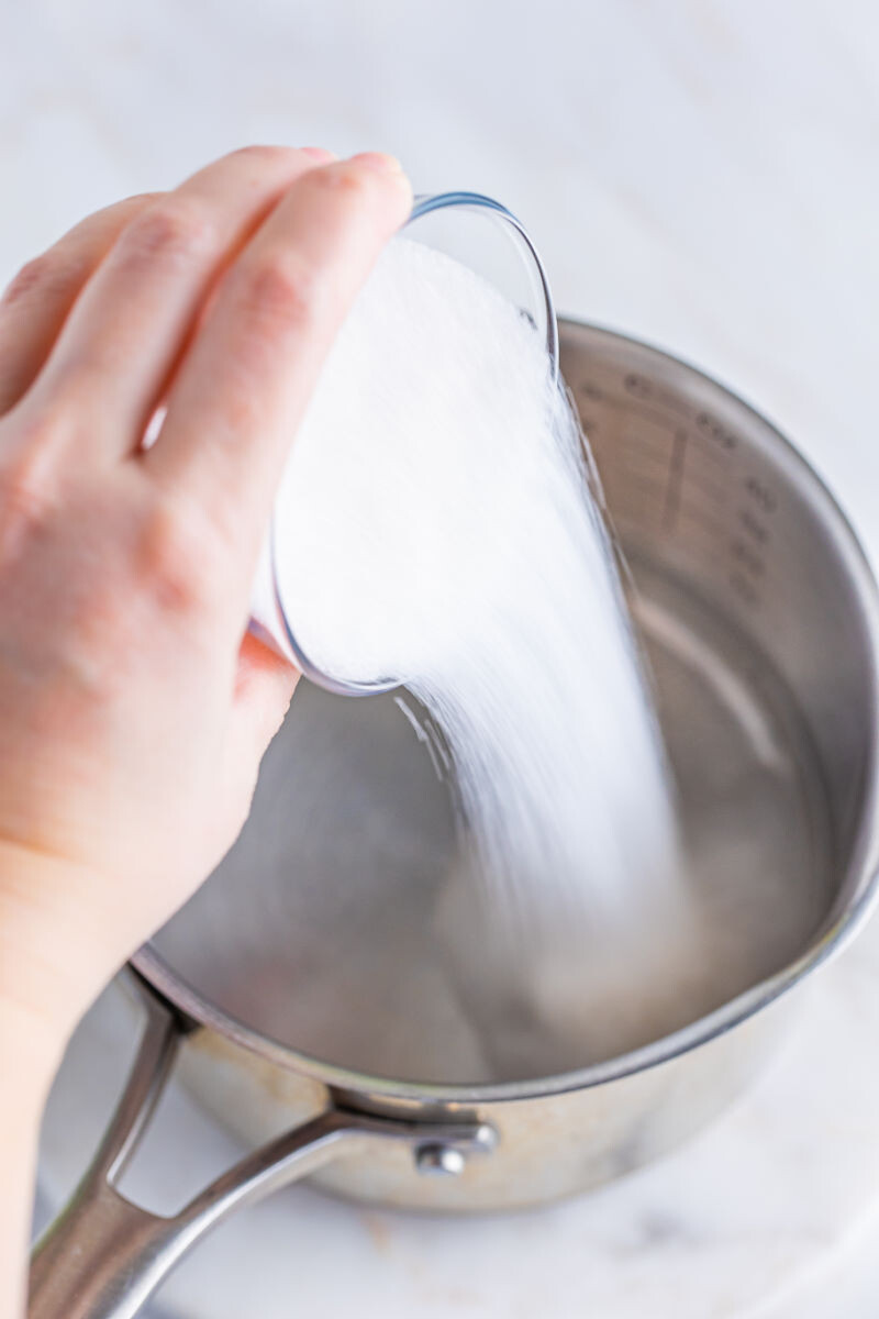 sugar being poured into a pot with water