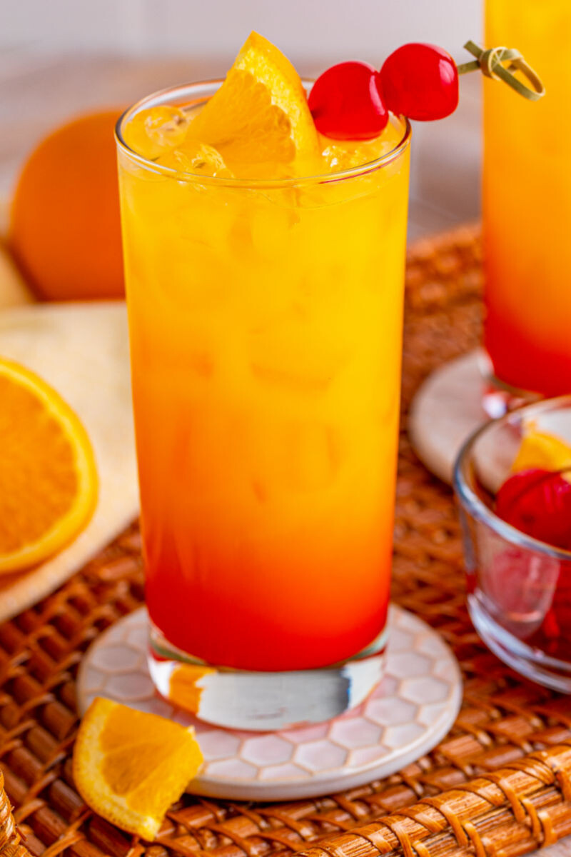 close up of a tequila sunrise cocktail on a wicker serving tray