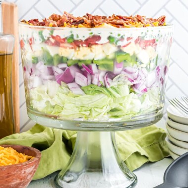 square image of 7 layer salad in a trifle bowl topped with cheese and bacon