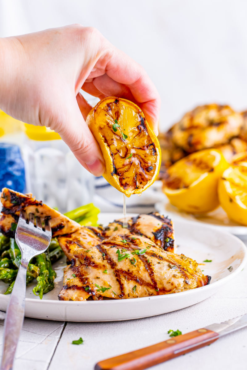 grilled lemon being squeeze over lemon garlic grilled chicken thighs on a plate