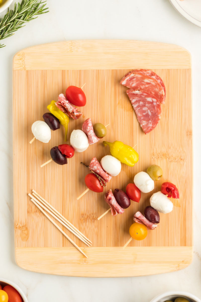 five assembled antipasto skewers on a cutting board next to more salami and skewers