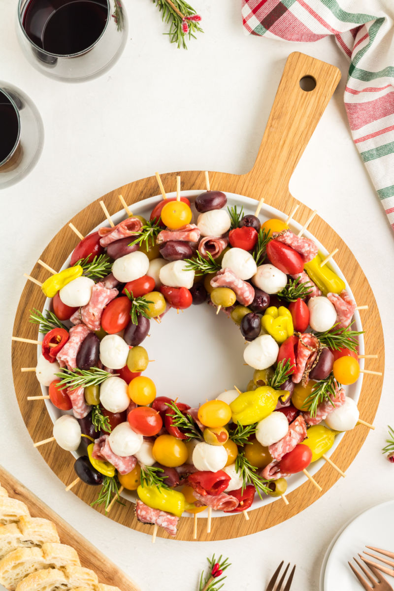 looking down at an antipasto skewers wreath on a white platter placed on a wooden serving board