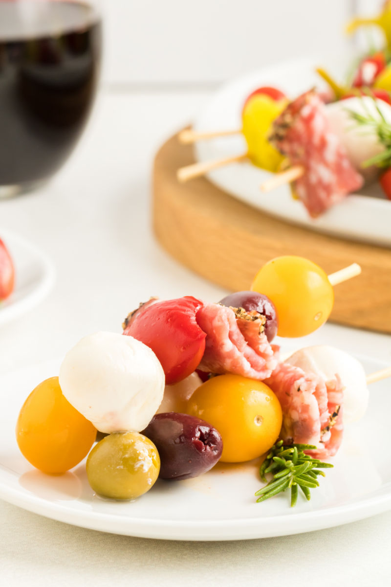 three antipasto skewers on a small plate with a sprig of fresh rosemary