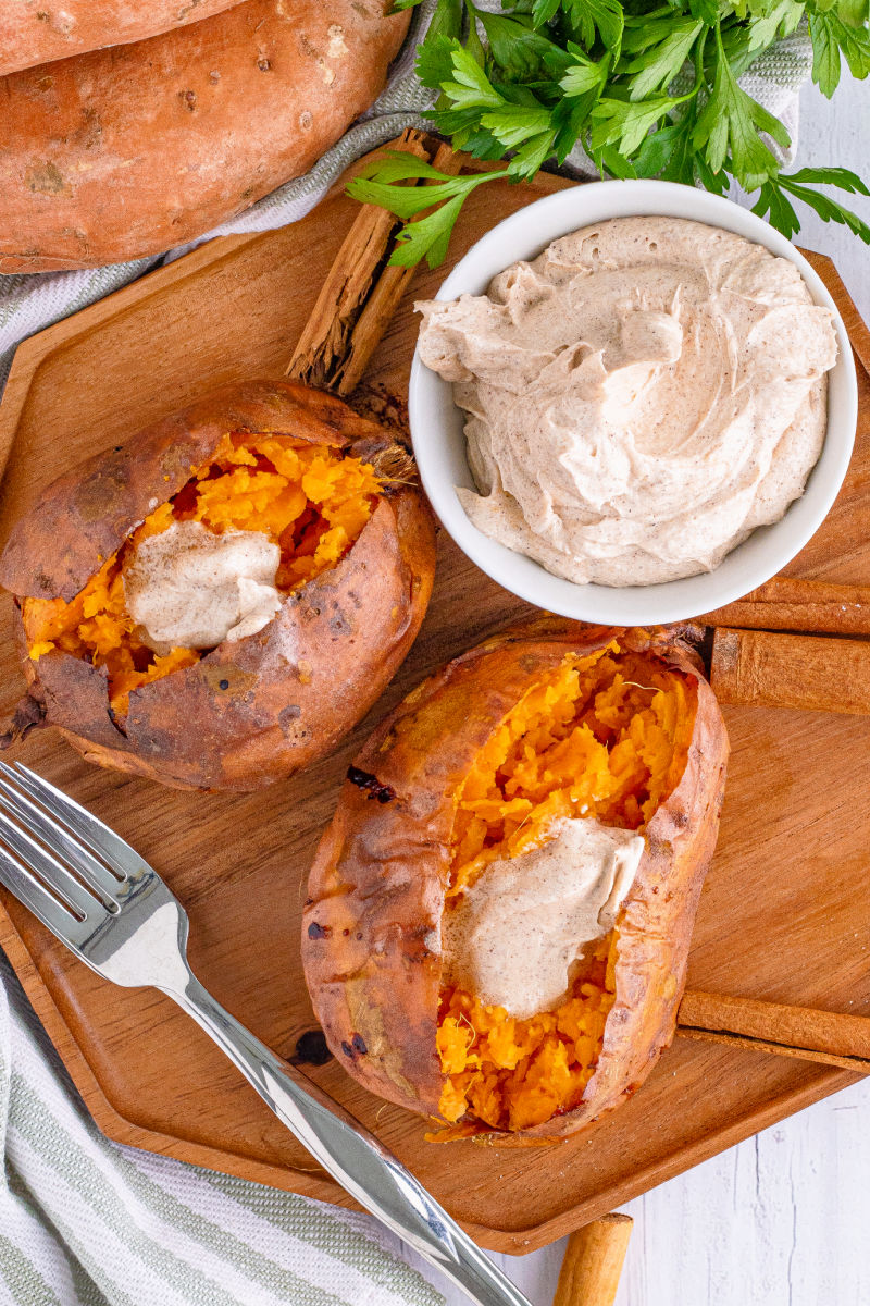 looking down at two baked sweet potato topped with cinnamon butter next to the bowl of butter on a wooden tray
