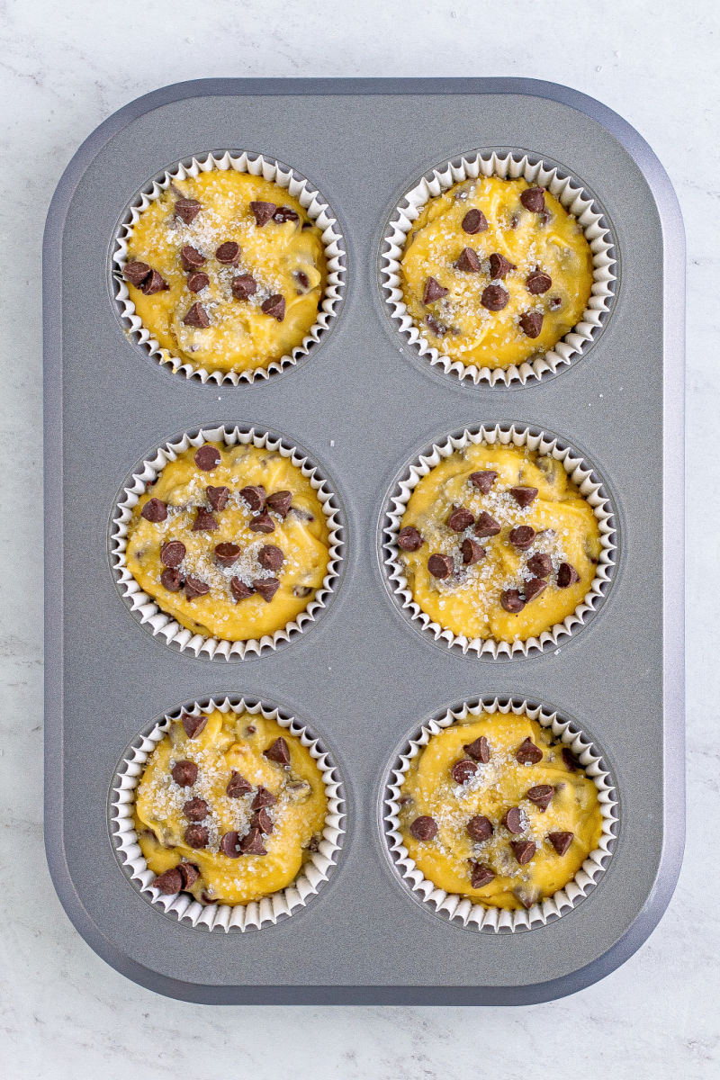 chocolate chip muffin batter in jumbo muffin tin cups with chocolate chips and decorating sugar on top
