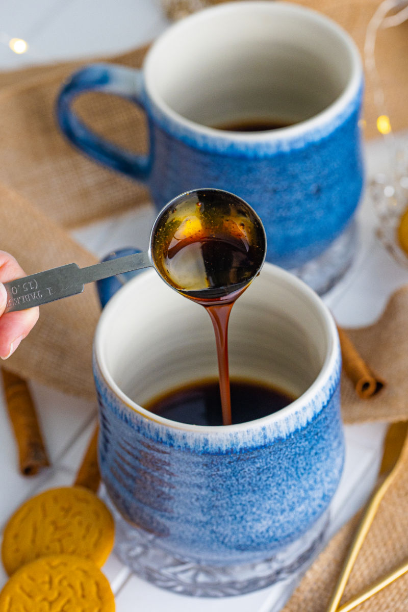 measuring spoon of gingerbread syrup being poured into a mug with coffee