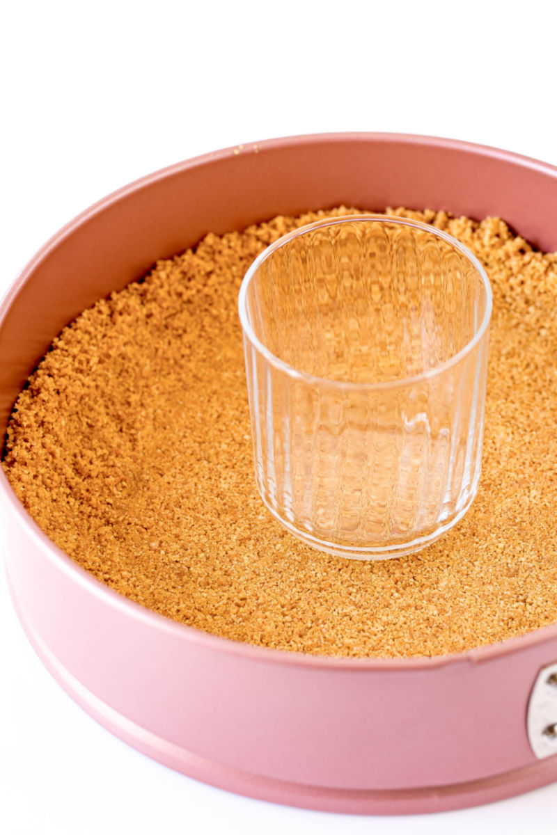 graham cracker crust pressed into the bottom of a springform pan with a drinking glass