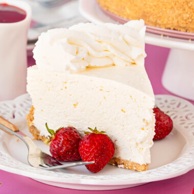 square image of a slice of no bake cheesecake on a plate with a fork and strawberries