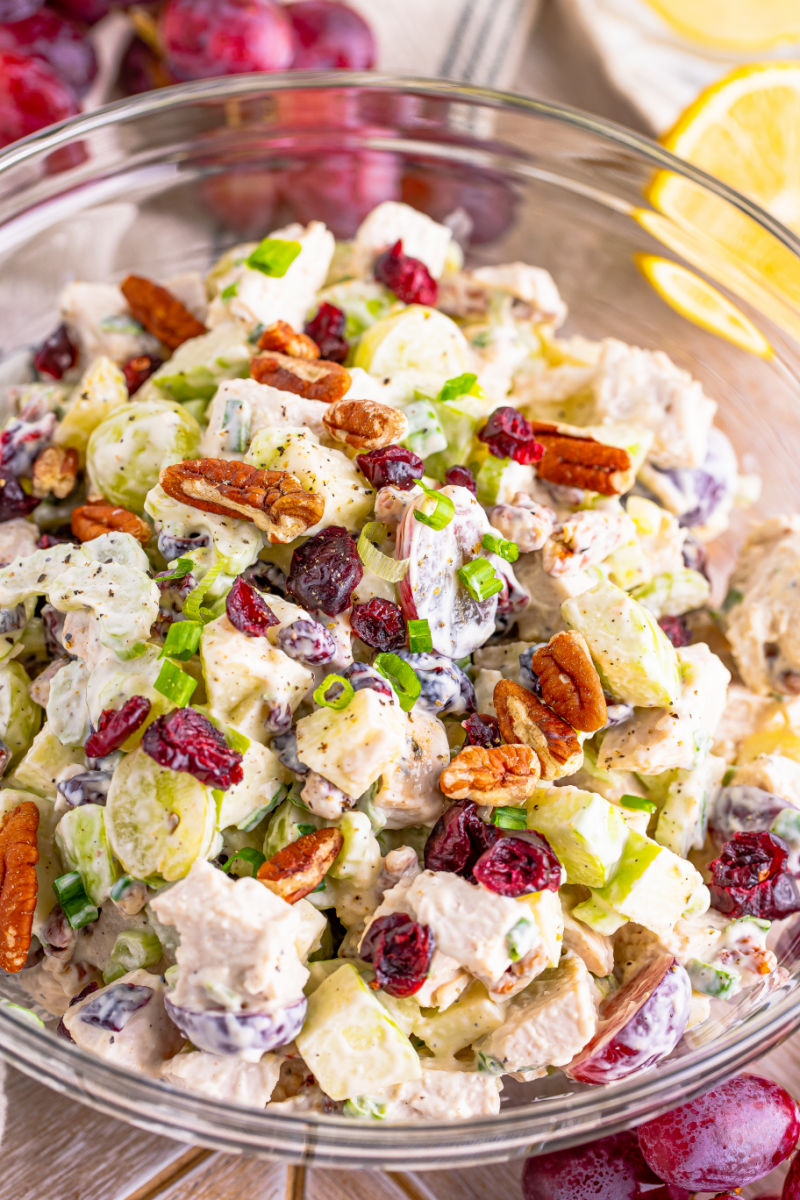 close up of turkey waldorf salad in a glass bowl with extra pecans and green onions on top