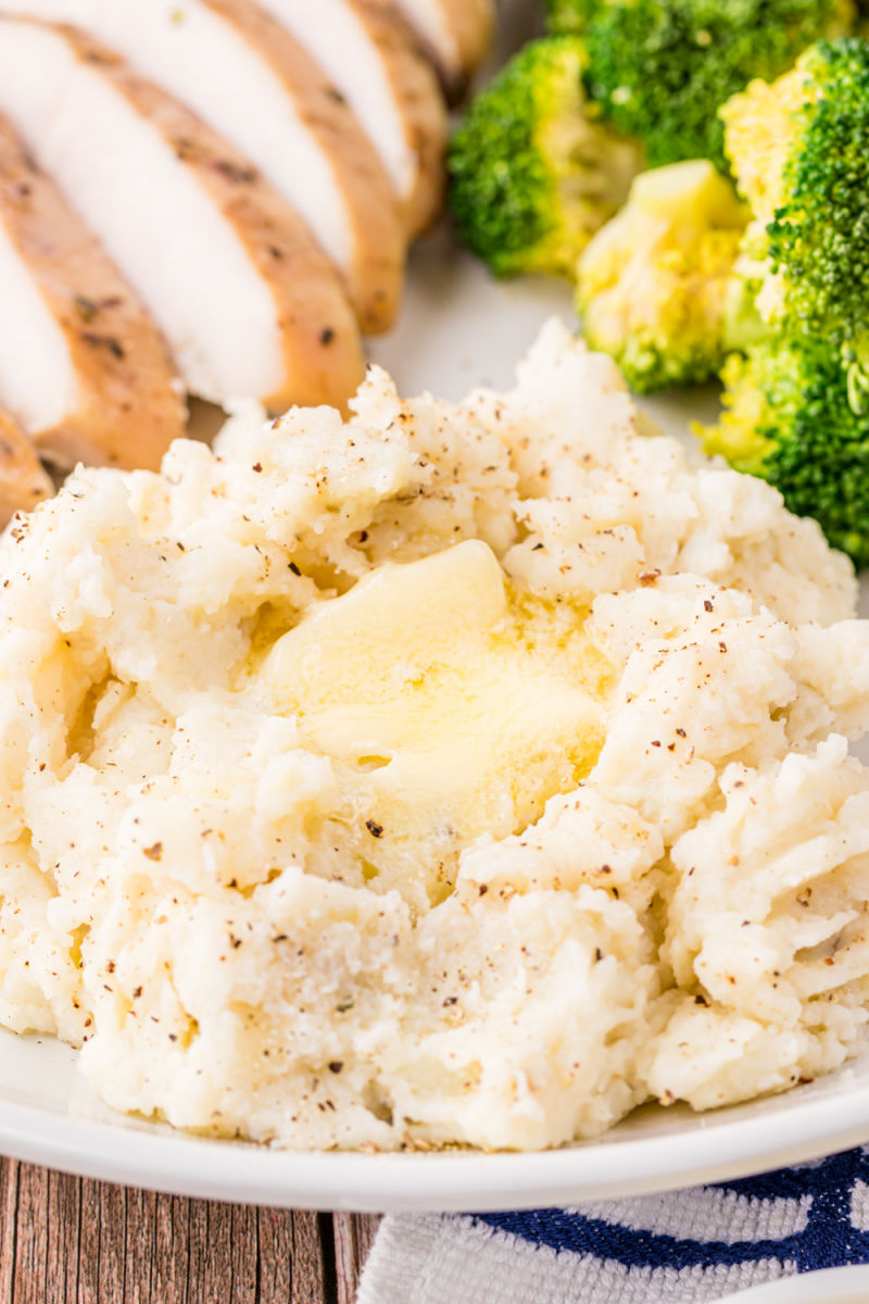close up of a a serving of mashed potatoes with butter on a dinner plate with chicken and broccoli