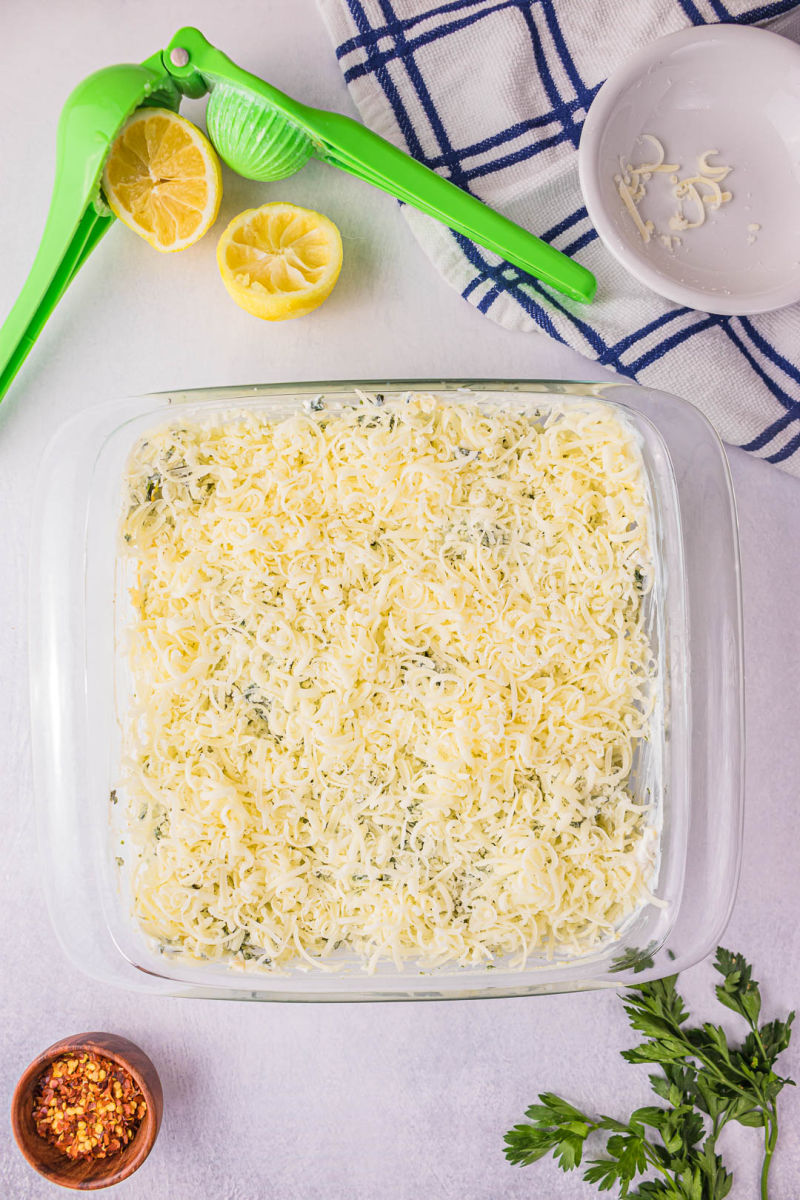 spinach artichoke dip in a square baking dish topped with shredded cheese