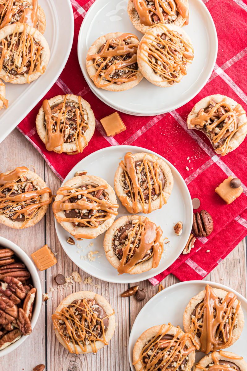 small plates of turtle cookie cups next to a bowl of pecans