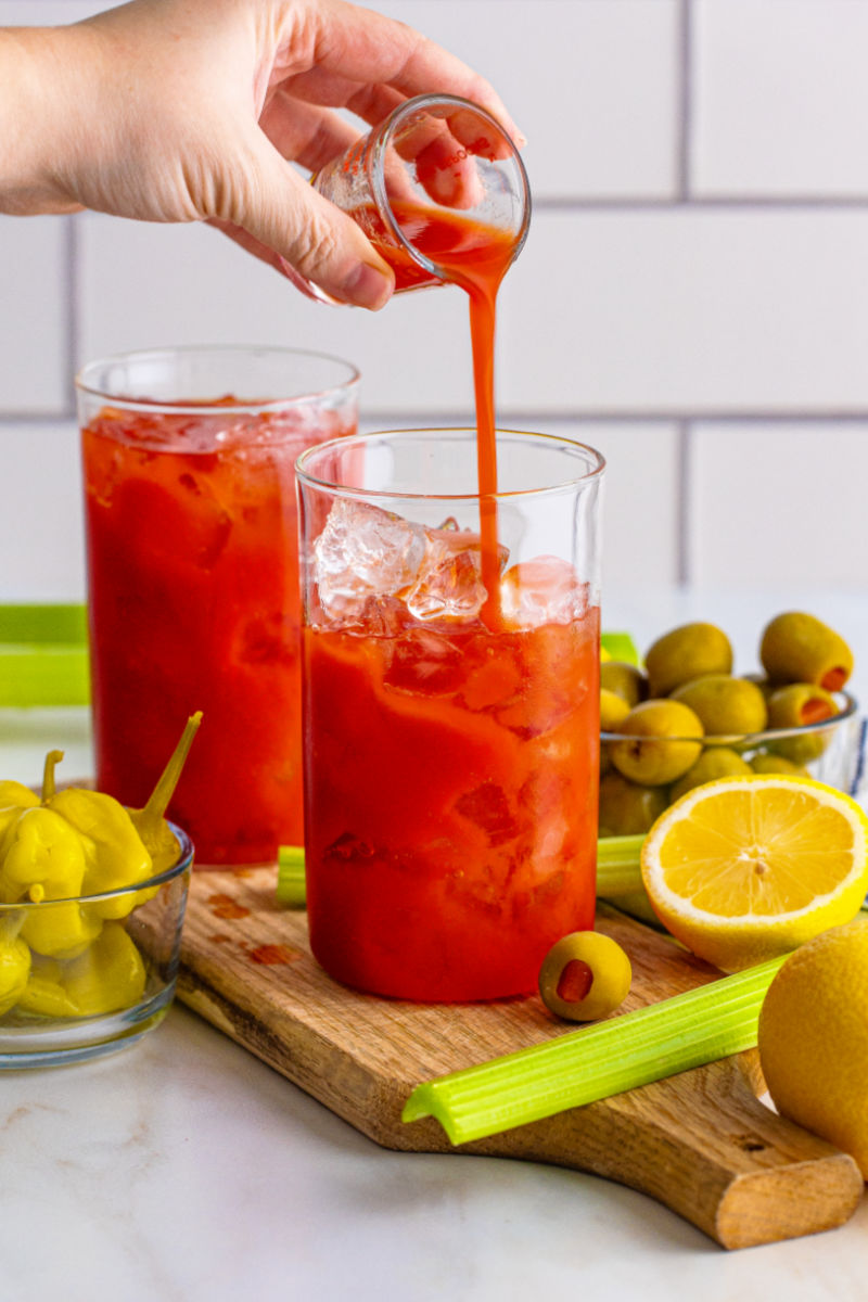 tomato juice being poured into a glass with vodka and ice