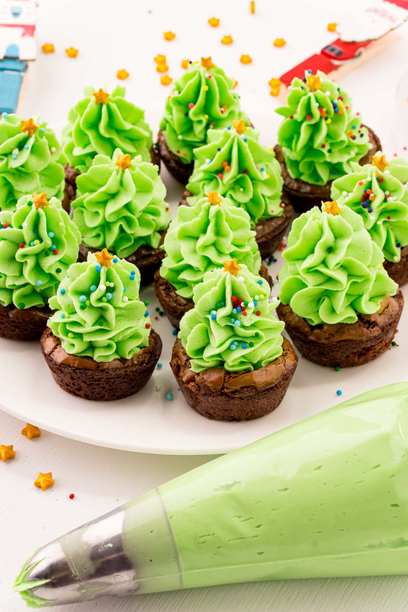 brownies cups topped with green buttercream in a tree shape next to the piping bag