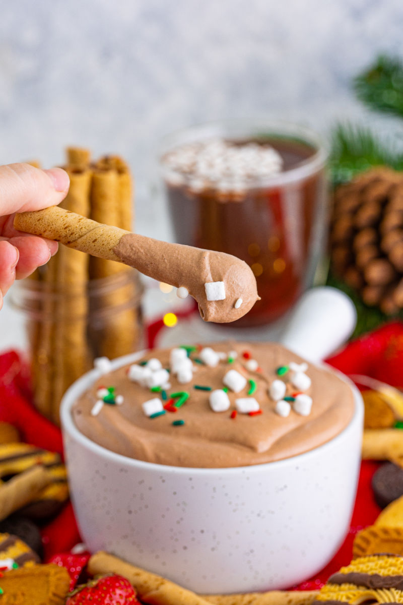 pirouette cookie with hot cocoa dip being held above the bowl