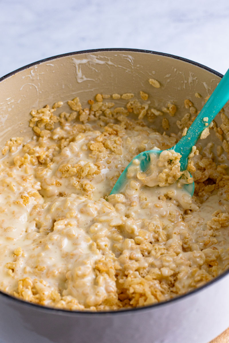 rice krispies being mixed into melted butter and marshmallows in a large pot