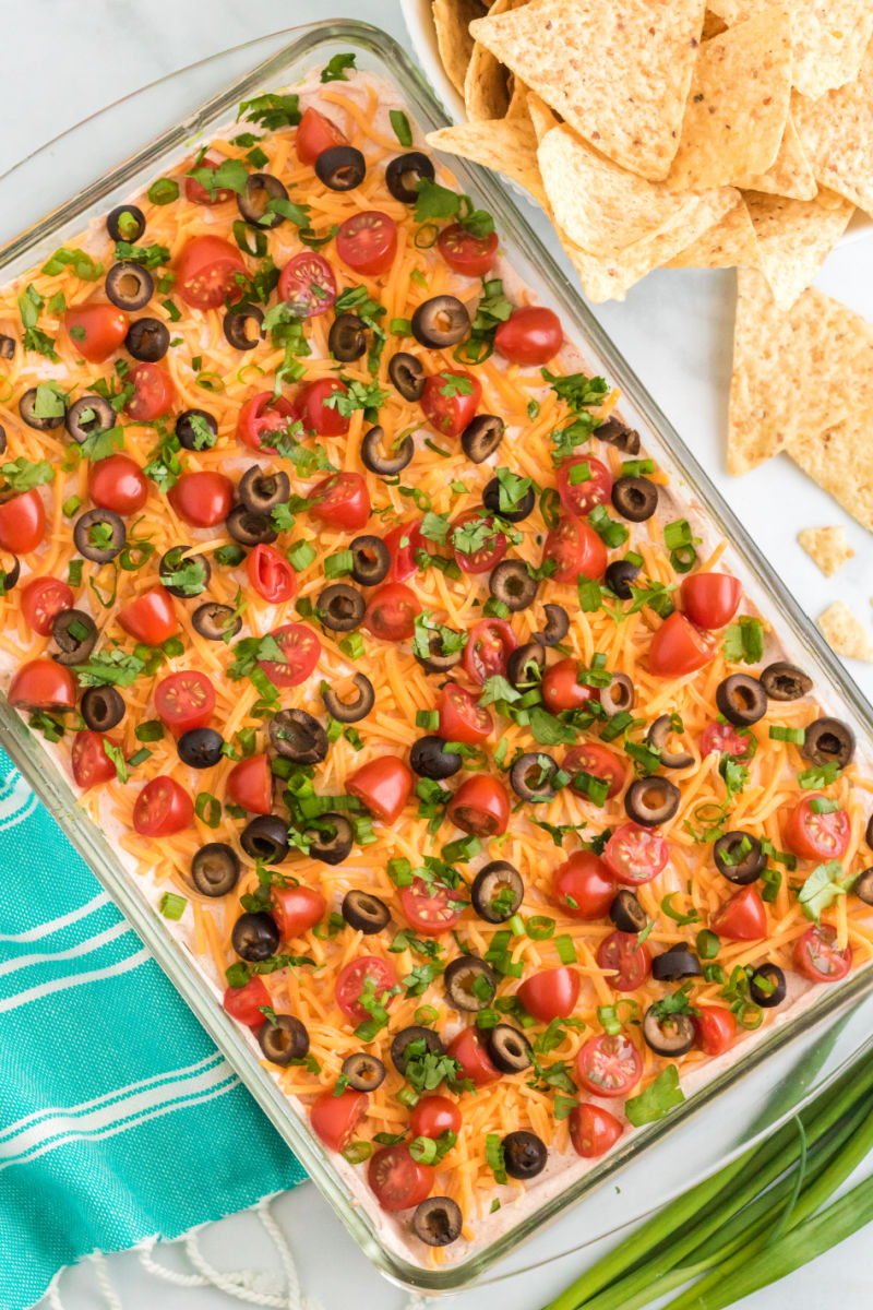 looking down at 7 layer dip topped with tomatoes, olives, green onion, and cilantro