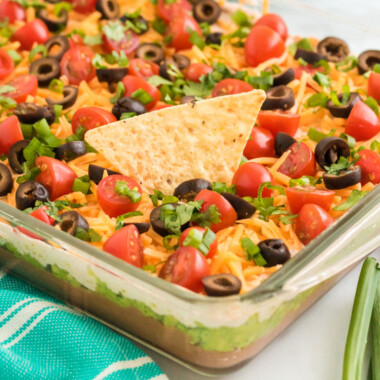 square image of 7 layer dip with a tortilla chip stuck into the dish