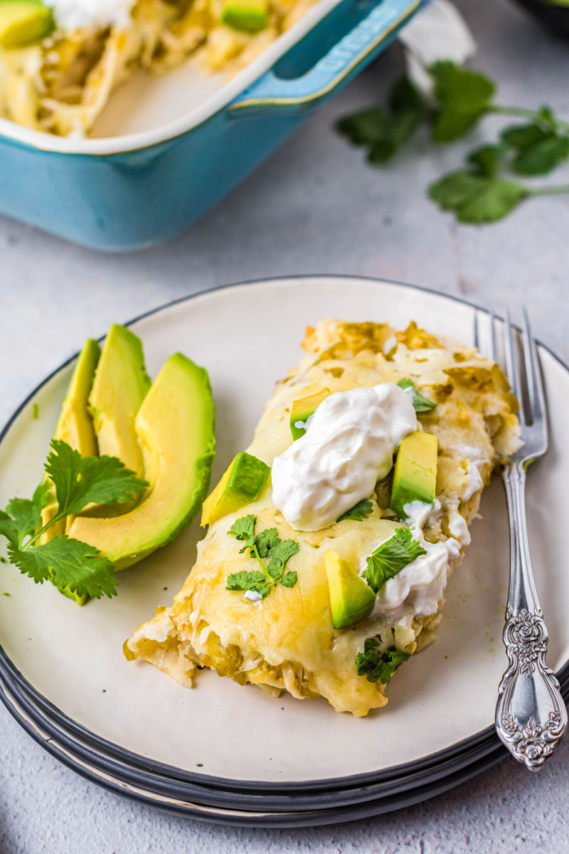 two green chicken enchiladas on a plate with avocado slices