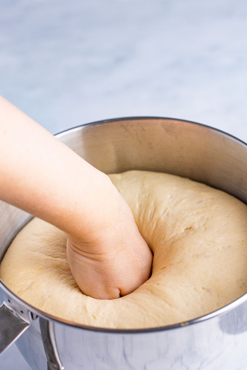 hand punching dough white bread dough in a stand mixer bowl after its first rise