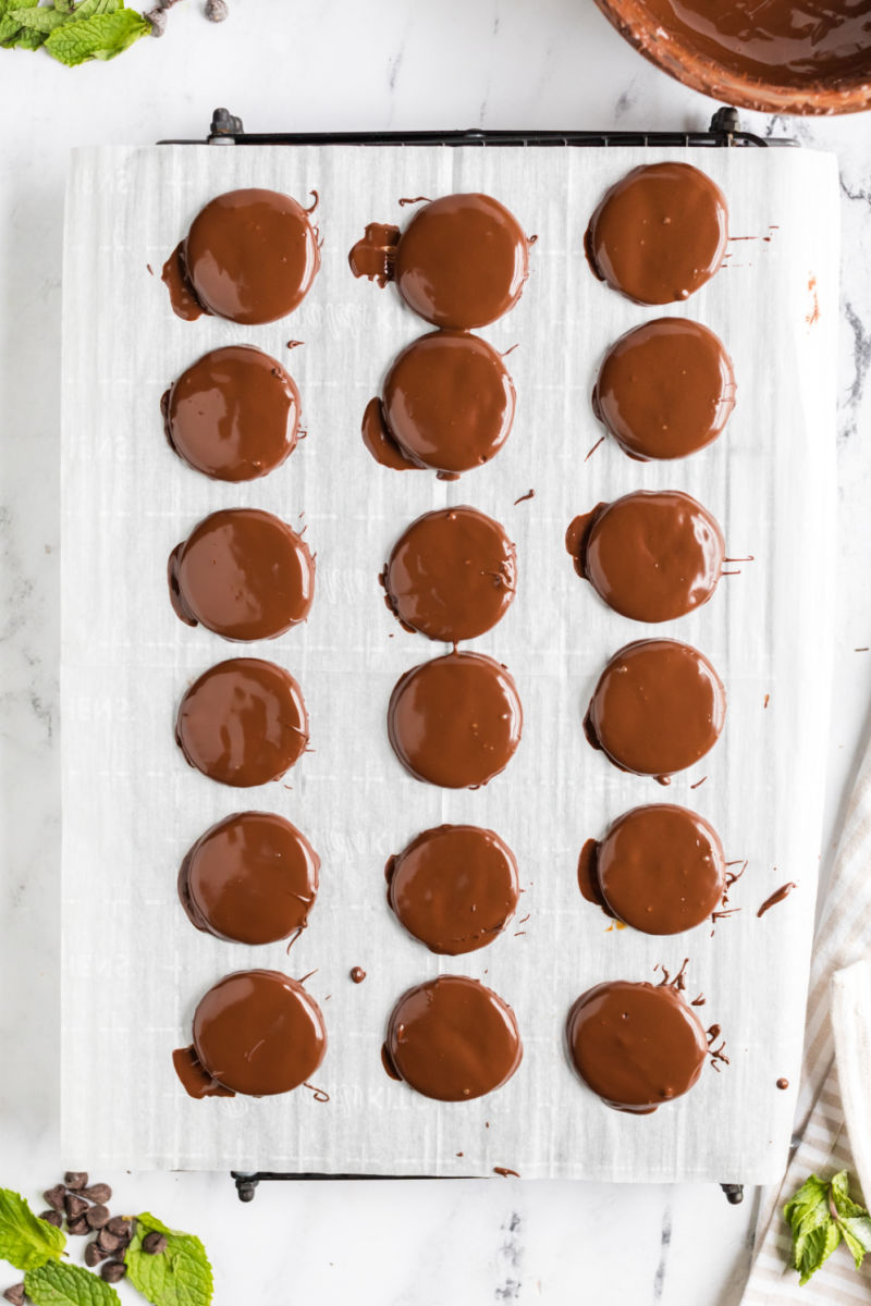 copycat thin mint girl scout cookies on a parchment paper lined baking sheet after being dipped