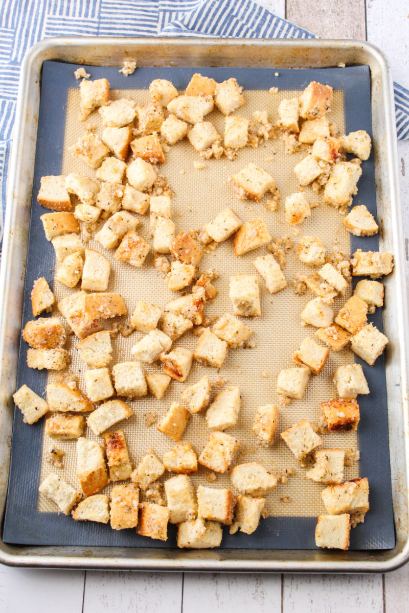 coated french bread cubes spread out on a lined baking sheet
