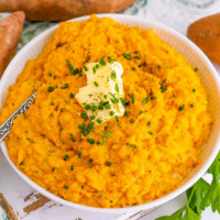 square image of mashed sweet potatoes in a bowl with pats of butter and chopped herbs
