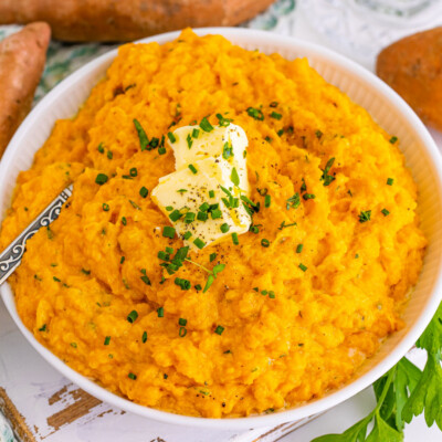 square image of mashed sweet potatoes in a bowl with pats of butter and chopped herbs