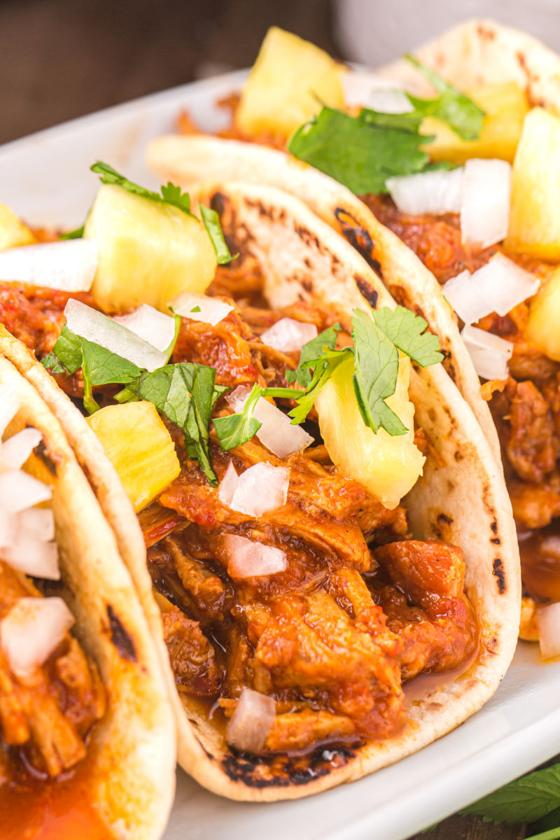 close up of al pastor tacos with onion, pineapple and cilantro on top
