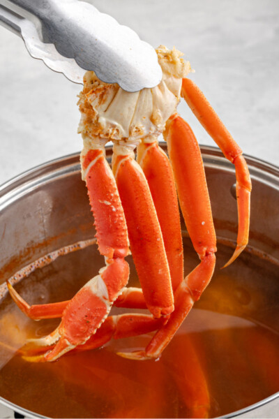 boiled snow crab leg cluster being lifted from a pot of seasoned water by tongs