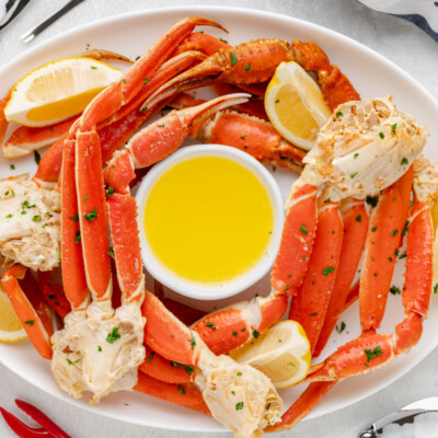 square image of snow crab legs on a platter with lemon wedges and bowl of clarified butter