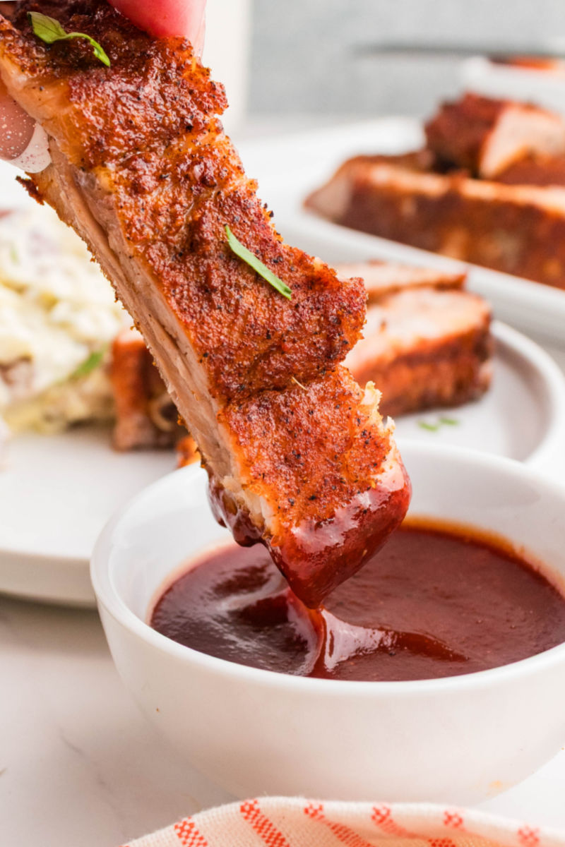 dry rub rib being dipped into a small bowl of BBQ sauce