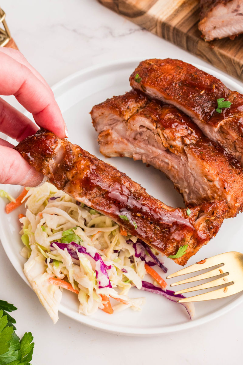 hand picking up a dry rub rib from a plate with ribs and coleslaw