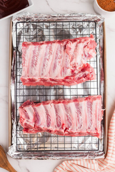 two half racks of ribs, bone side up, on a wire rack over a foil lined baking sheet
