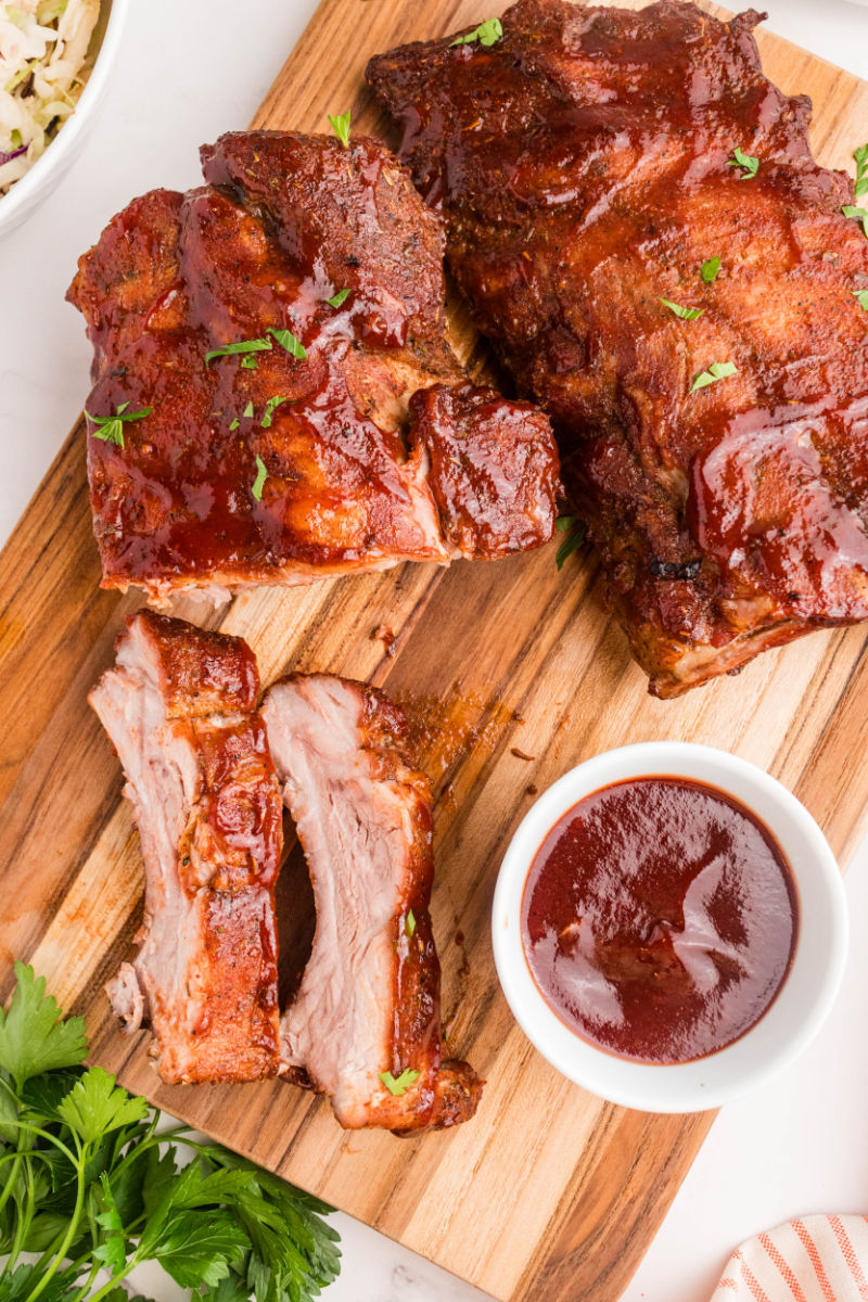 cooked dry rub ribs with BBQ sauce on a cutting board next to a bowl of sauce