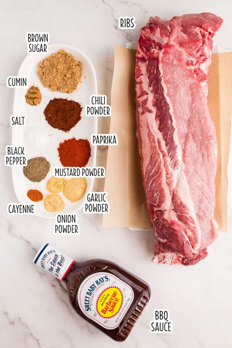 ingredients to make dry rub for rib, baby back ribs, and a bottle of bbq sauce laid out on a counter with text labels