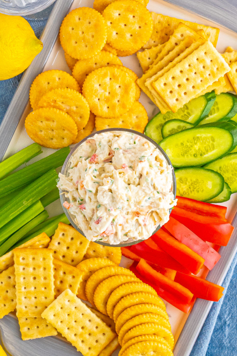 looking down at a bowl of chilled crab dip on a tray with veggies and crackers for dipping