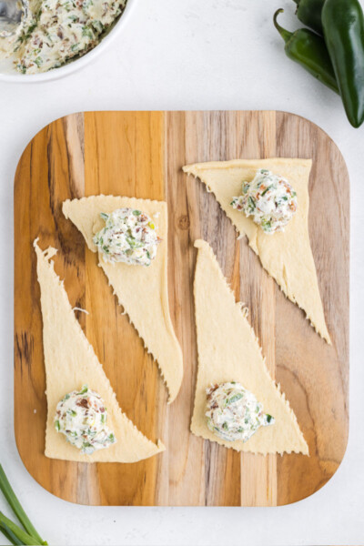 scoops of jalapeno popper bite filling on the wide end of crescent roll dough triangles