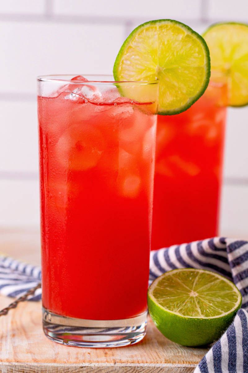 two bay breeze drinks on a wooden board next to half of a lime
