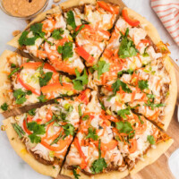 square image of a thai chicken pizza cut into slices on a cutting board
