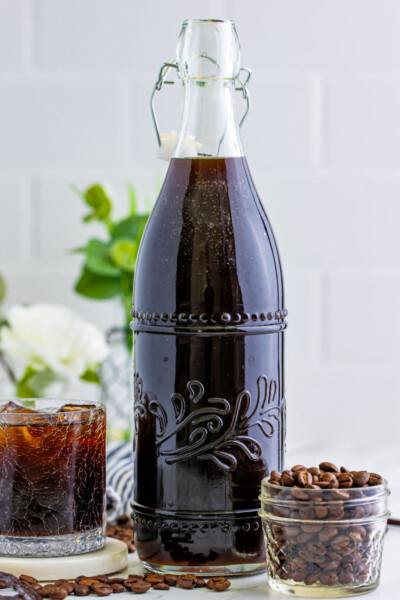 homemade coffee liqueur in a swing top bottle next to a glass of kahlua and a jar of coffee beans