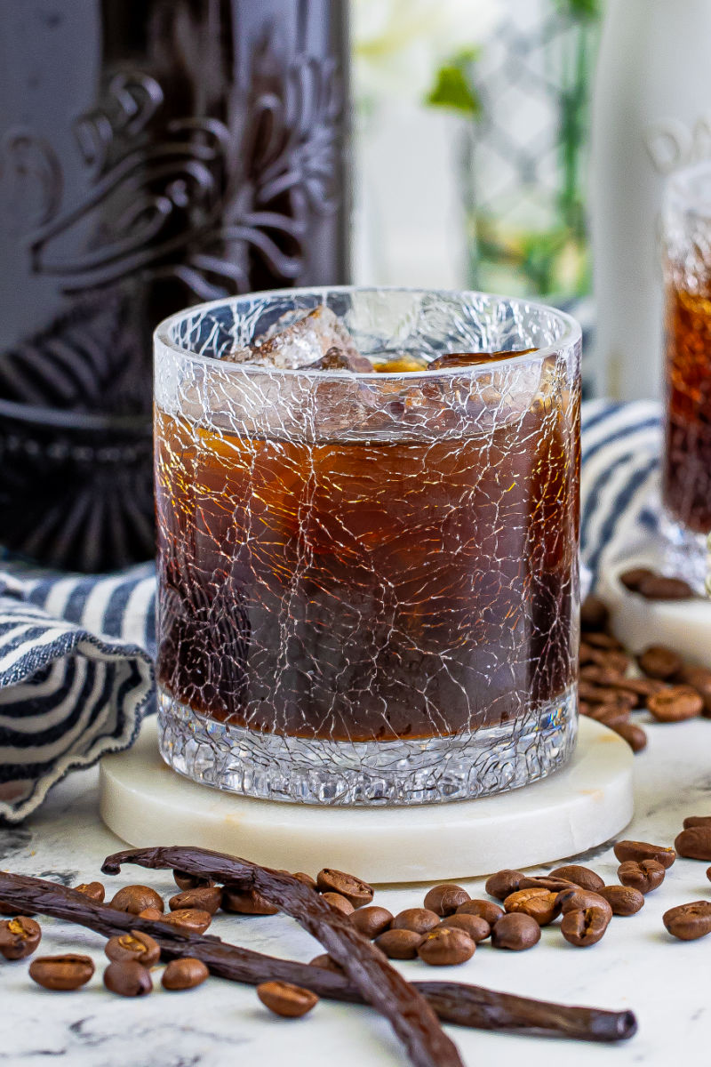 a glass of homemade kahlua over ice next to vanilla pods and coffee beans